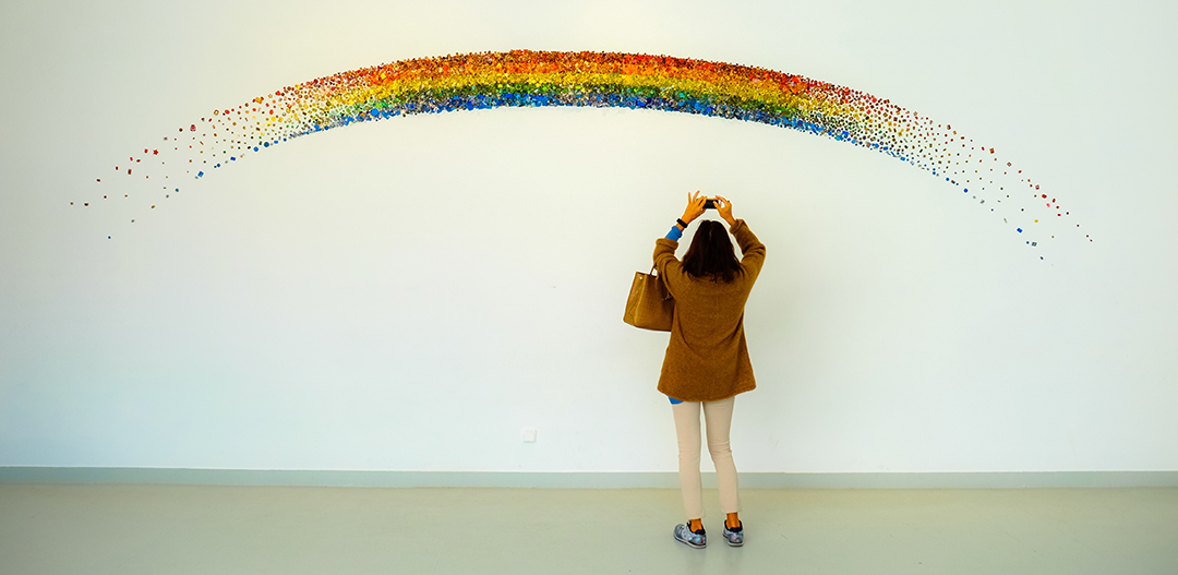 woman taking picture of rainbow wall art.